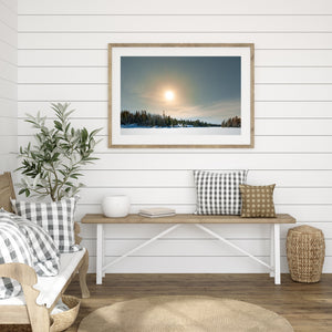 Clear winter sky and glowing sun above an Ontario forest shoreline