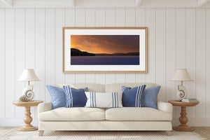 Quiet frozen lake bordered by wooded hills under a colourful sunset
