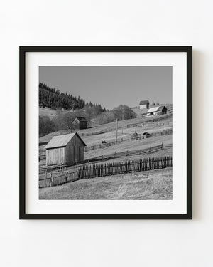 Wooden farm buildings and fences on a Romanian hillside in black and white