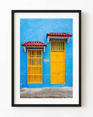 Yellow door and barred window against a bright blue wall in Bogotá
