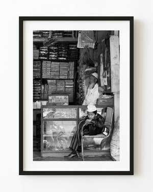 Young boy seated inside a crowded Indian shop in black and white