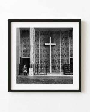 Zagreb vendor seated beneath a large church cross in black and white