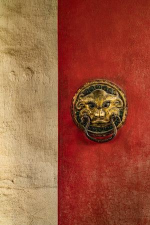Weathered gold face knocker with iron ring on cracked red paint