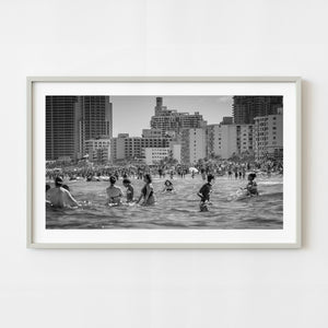 Crowded South Beach Miami scene with swimmers and beachfront buildings in black and white
