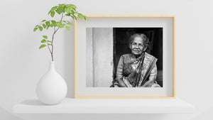 Indian woman seated in doorway with patterned saree and gray hair
