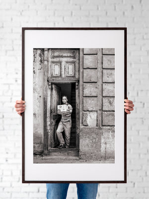 Man framed by cracked wooden doorway and weathered Cuban architecture