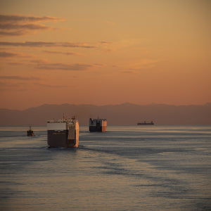 Golden evening light over cargo ships, blue-grey water and a mountain horizon in Japan.