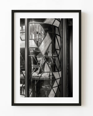 Seated man seen through an ornate London pub window with geometric glass and street reflections.