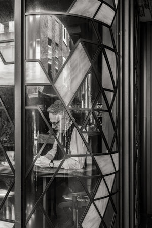 Black and white London photograph layering a pub interior with reflected brick buildings.
