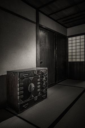 Black and white Japanese interior with an old chest, sliding wooden doors and a glowing shoji screen.
