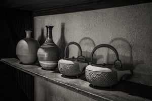 Two Japanese iron kettles cast curved handle shadows on a textured wall.