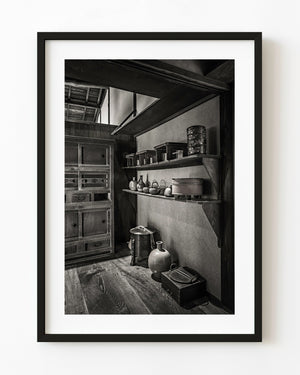 Historic kitchen shelves with vessels and wooden stands at Matsue's Samurai Residence, Japan, in black and white.