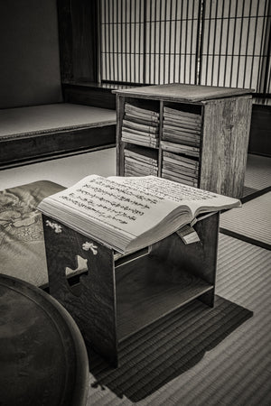 Japanese text on open pages and bound volumes beneath gridded shoji screens, photographed in black and white.