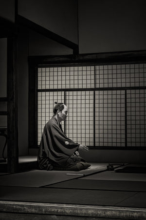 Black and white Japanese interior with a historical samurai figure seated before shoji screens.