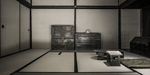 Black and white Japanese interior with storage chests along a plain wall and an open book.