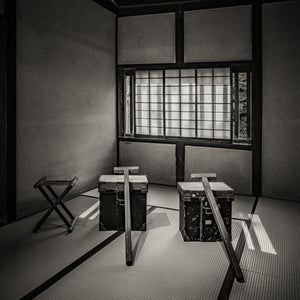 Black and white still life of Japanese carrying chests beneath a gridded paper window.