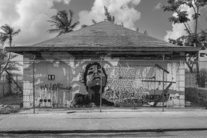 Graffiti face behind chain link fence on weathered Nassau building