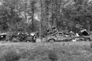 Abandoned pickup truck surrounded by wrecked vehicles and forest