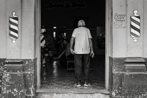 Santa Marta barber shop entrance with older man and painted barber poles