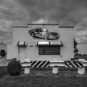 Faded sports car mural painted across a roadside brick building