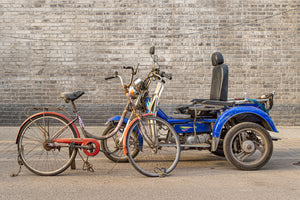 Weathered bicycle and three wheeled vehicle against brick wall