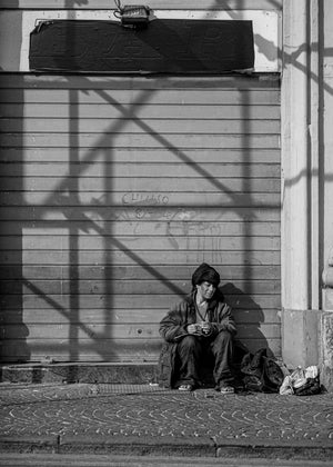 Woman seated outside a closed Naples storefront in hard sunlight