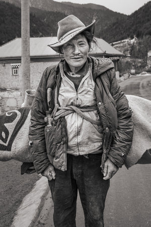 Tibetan traveler wearing weathered hat beside pack animal