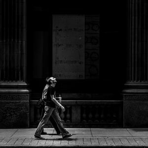 Black and white Bay Street photograph with a sunlit pedestrian beneath a dark stone facade.