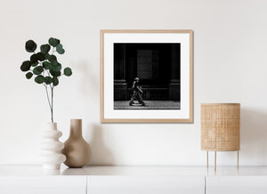 Plywood covers a window between large columns above a man walking in downtown Toronto.