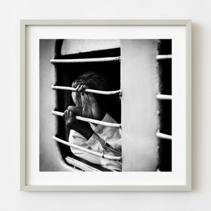 Black and white photograph of a train passenger covering their face behind a barred window in Mysore India