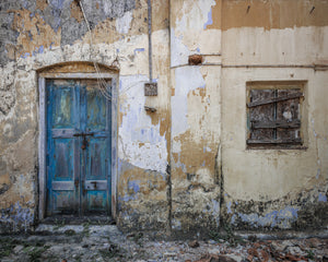 Peeling plaster facade with blue door and boarded window
