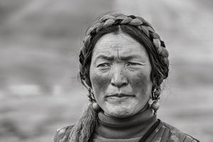 Weathered Tibetan woman with braided hair and traditional earrings