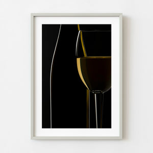 White wine glass beside a dark bottle on black