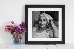 Indian woman seated in floral clothing with one arm raised beside her face