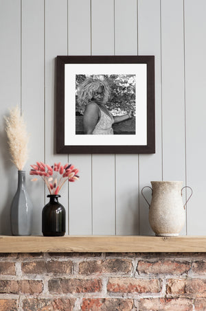 Woman with voluminous light wig framed by dense leaves and branches