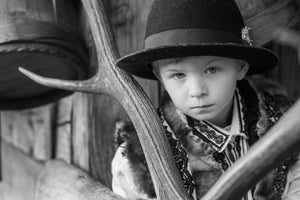 Black-and-white portrait of a boy wearing a broad dark hat and patterned clothing