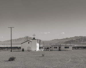 Monochrome photograph of a small abandoned Route 66 church and distant desert ridges.