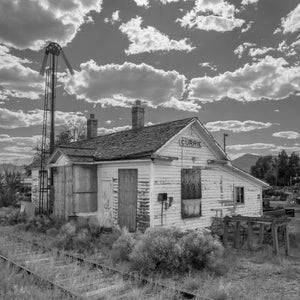 Weathered Currie station with boarded windows, railway tracks and a tall signal.