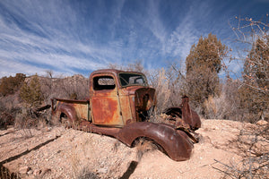Colour photograph of a weathered pickup truck on dry desert ground.