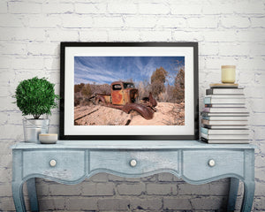 Orange and brown rust covers an abandoned desert truck beneath wispy clouds.