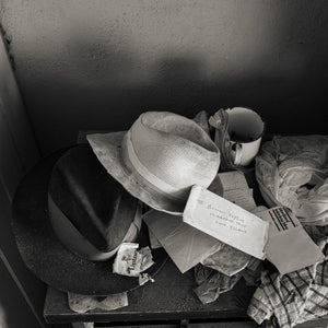 A pale woven hat rests above a darker hat on a cluttered table in an abandoned Bahamas home.