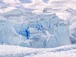 Deep blue openings between Antarctic ice walls with rounded snowy ridges behind.