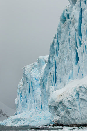 Pale ice ridges and blue crevices rising beside a grey Antarctic sky.