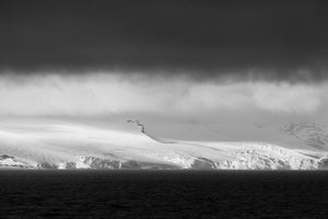 A pale Antarctic coastline stretches between dark water and a broad bank of cloud.