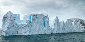 Pale Antarctic ice forms a broken wall beneath a cloudy sky.