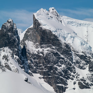 Square Antarctic mountain photograph with dark rock and sunlit snow.