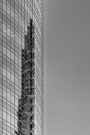 Black and white view of a glass building with a wavering reflection and plain sky.