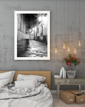 Tall stone walls enclose a narrow night passage with repeated lamps and reflected light.