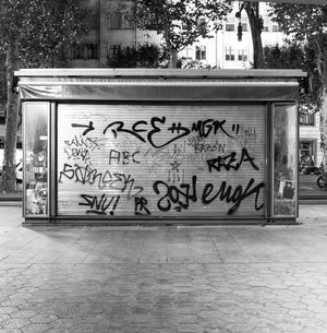 Layered graffiti covers a metal newsstand shutter above patterned pavement in Barcelona.