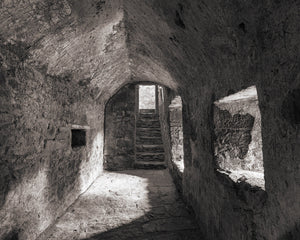 Monochrome view along Blarney Castle’s stone passage toward an arch and steps.